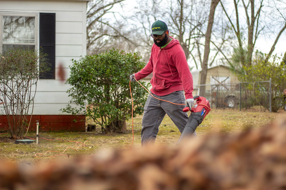 a man removes fall leaves from a yard with an electric leaf blower