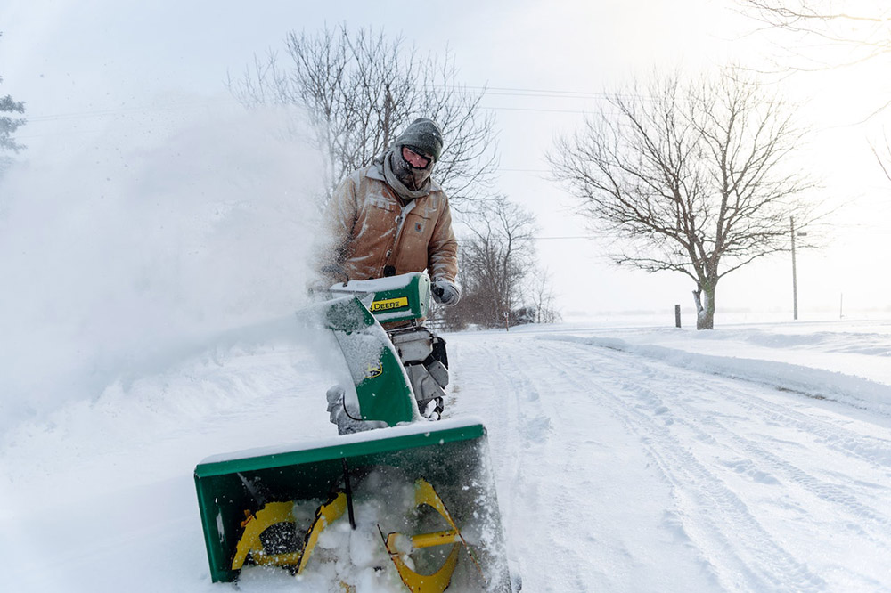 a person removes snow with a snow blower from a driveway